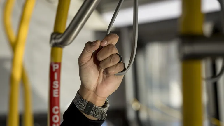 Closeup of a man holding a strap on a public bus.