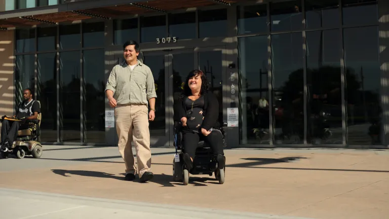  A man walks beside a woman using a wheelchair.