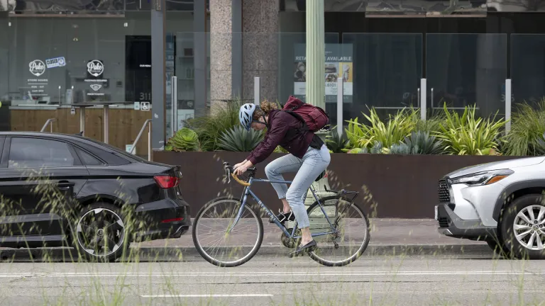 A cyclist commuter rides past parked cars in Oakland.