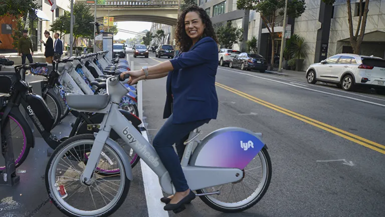 A smiling businesswoman astride a Bay Wheels e-bike.