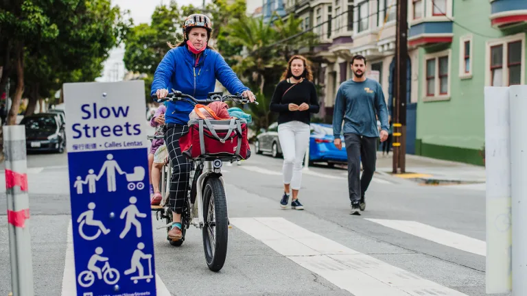 A cyclist with children on the back of the bike rides alongside people walking on a Slow Street in San Francisco.