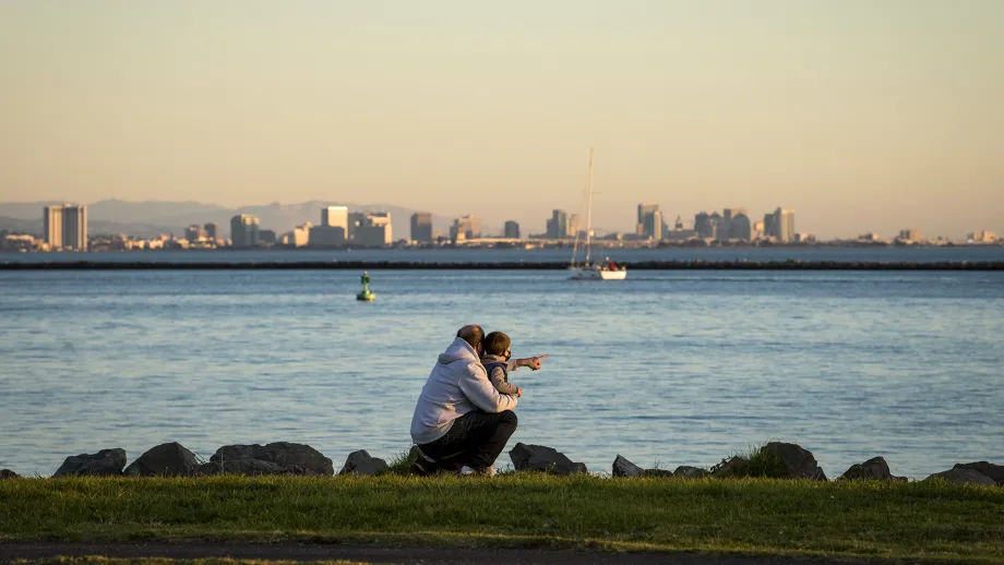 An adult and child pointing at the water, with the San Francisco skyline ahead.