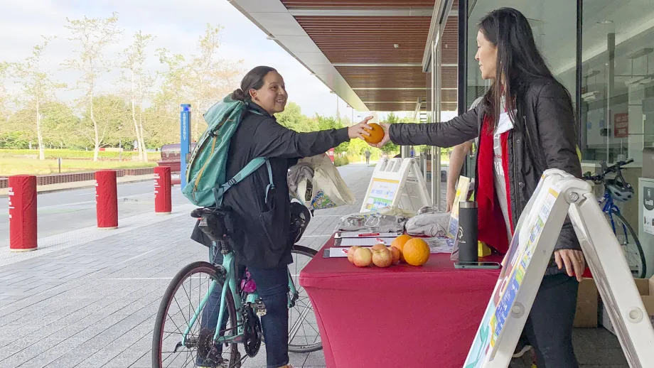 A Bike to Work Day volunteer hands an orange to a cyclist at an Energizer Station.