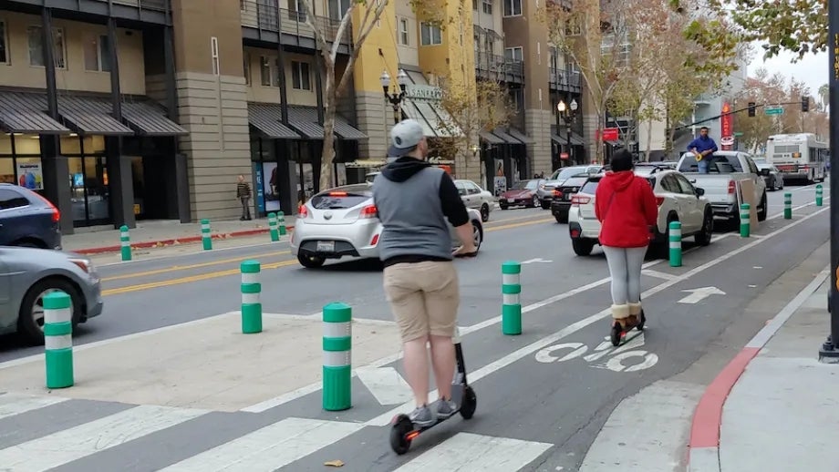 People riding electric scooters in a protected bike lane in San Jose.