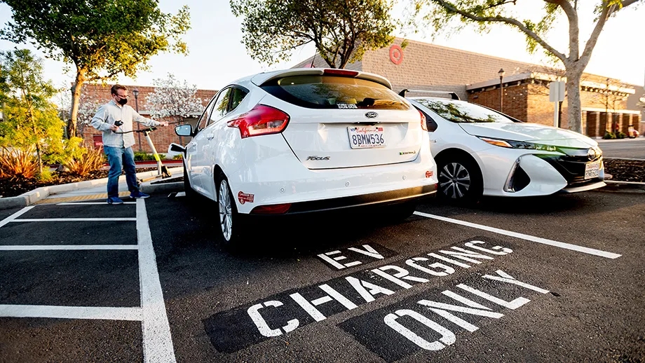 A man plugging in his electric vehicle in a designated parking lot space.