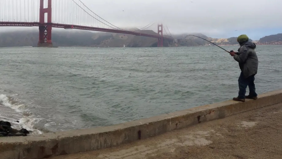 A fisherman with a view of a foggy Golden Gate Bridge.
