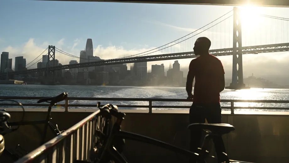 Silhouette of a ferry passenger next to onboard bike racks, as the boat passes under the San Francisco-Oakland Bay Bridge.